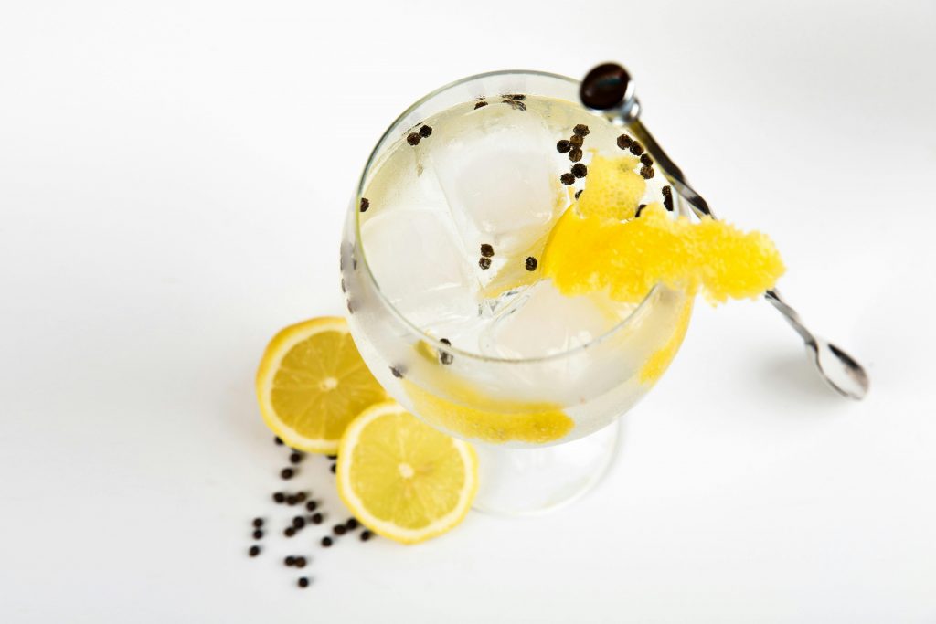Top view of a gin and tonic cocktail with lemon slices, ice, and peppercorn garnish.